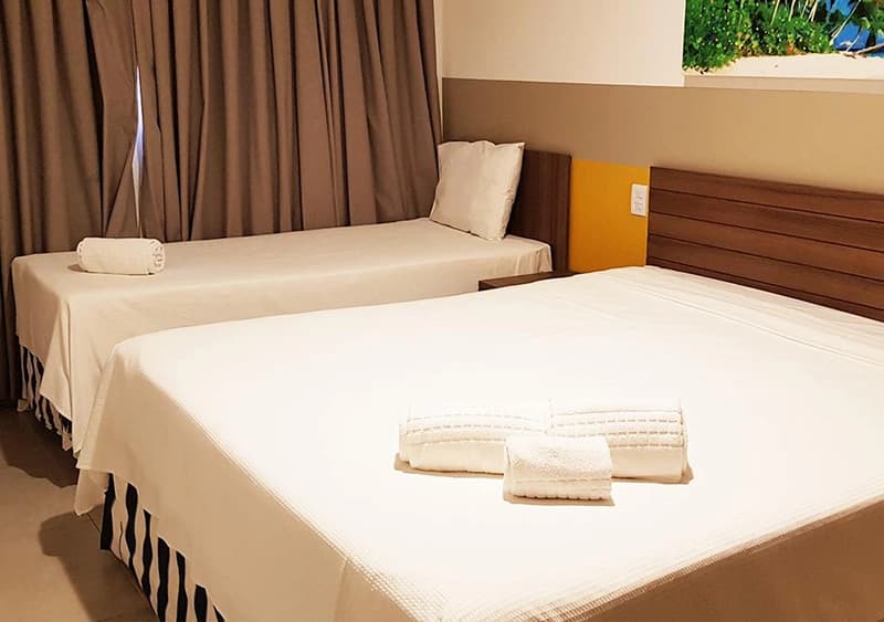 Quarto com cama de casal, lençóis brancos e cortinas.