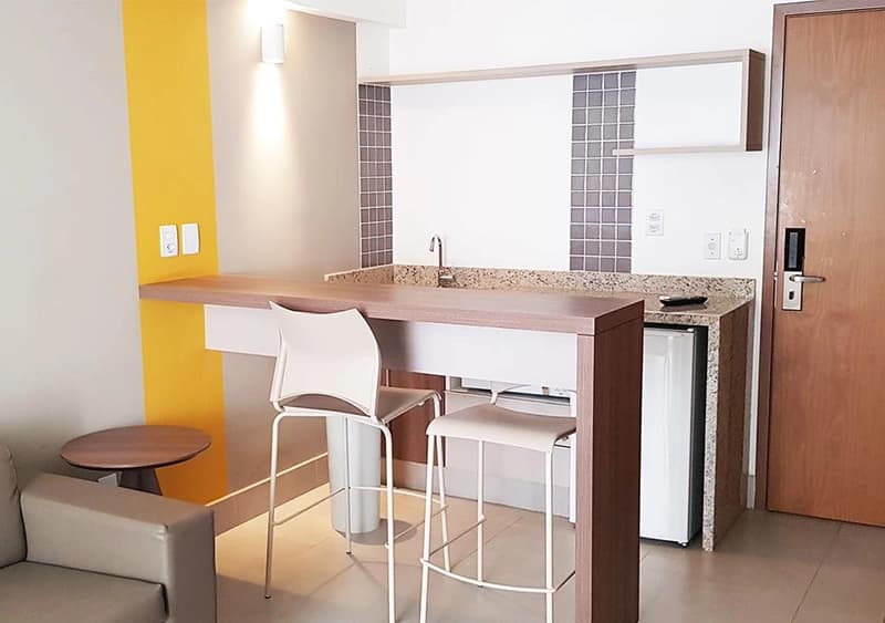 Cozinha compacta de um apartamento com bancada e banquetas brancas.