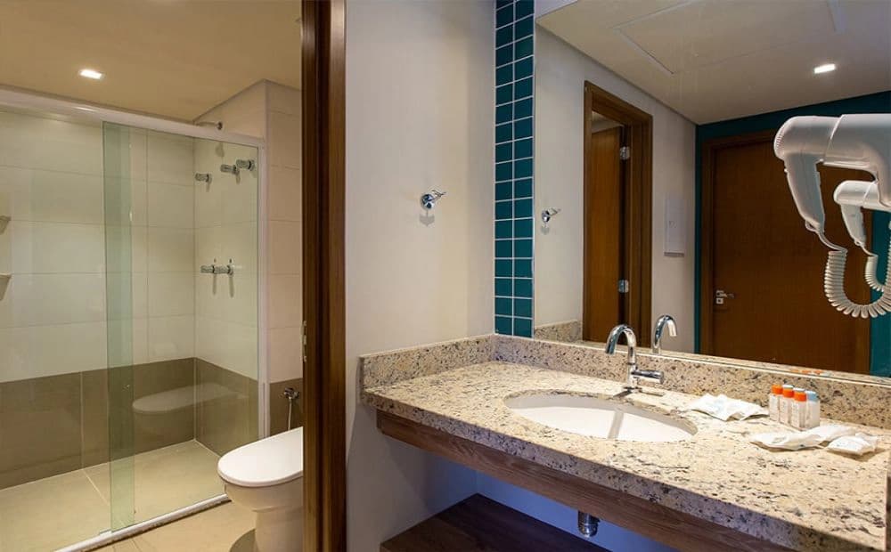 Banheiro de um apartamento com pia, espelho e box de vidro.