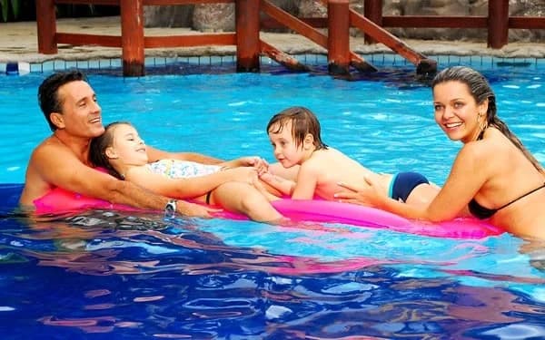 Área da piscina com hóspedes relaxando em espreguiçadeiras e dentro da água.