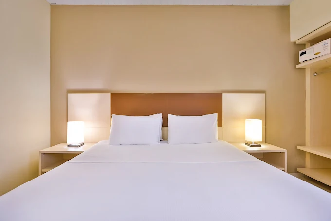 Quarto de hotel com cama de casal arrumada e lençóis brancos.