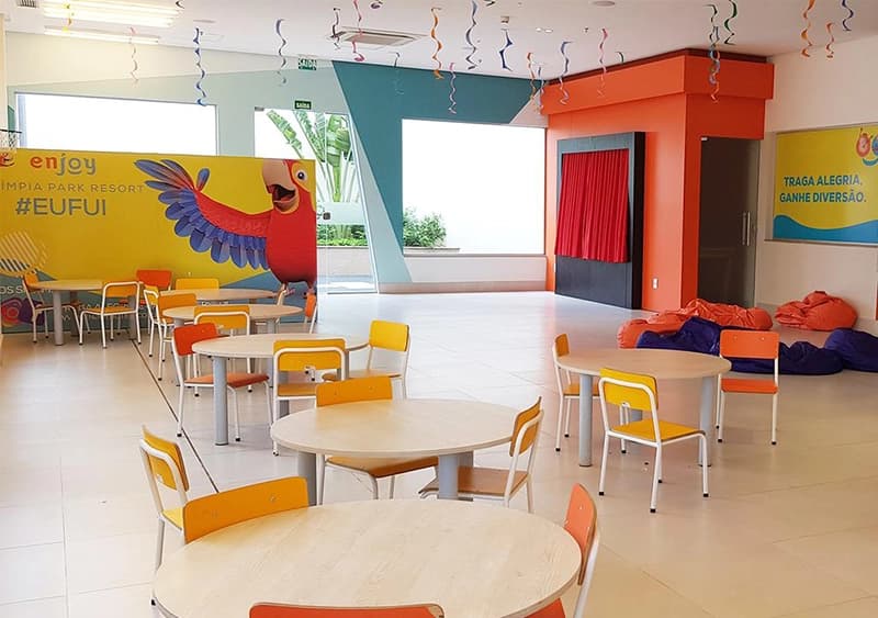 Espaço kids interno com mesas e cadeiras infantis coloridas.
