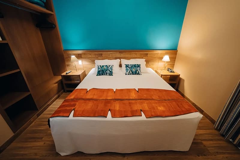 Quarto de hotel com duas camas, cabeceiras laranjas e iluminação azul.