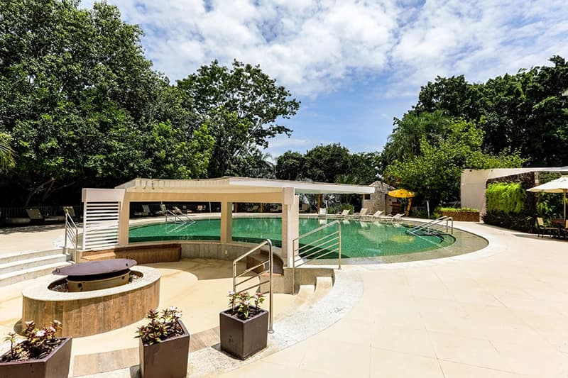 Área da piscina com espreguiçadeiras e o prédio do hotel ao fundo.