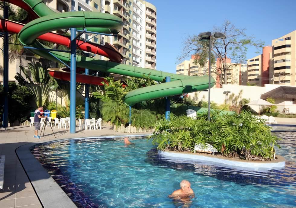 Crianças brincando na área infantil com escorregadores e jatos d'água.