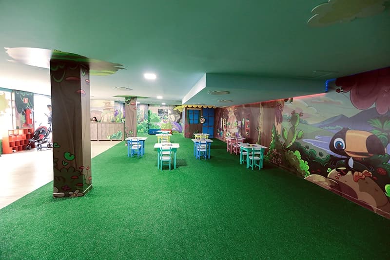 Área de recreação infantil interna, com piso verde e brinquedos.