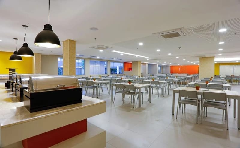 Amplo restaurante do hotel em estilo refeitório, com mesas e cadeiras.