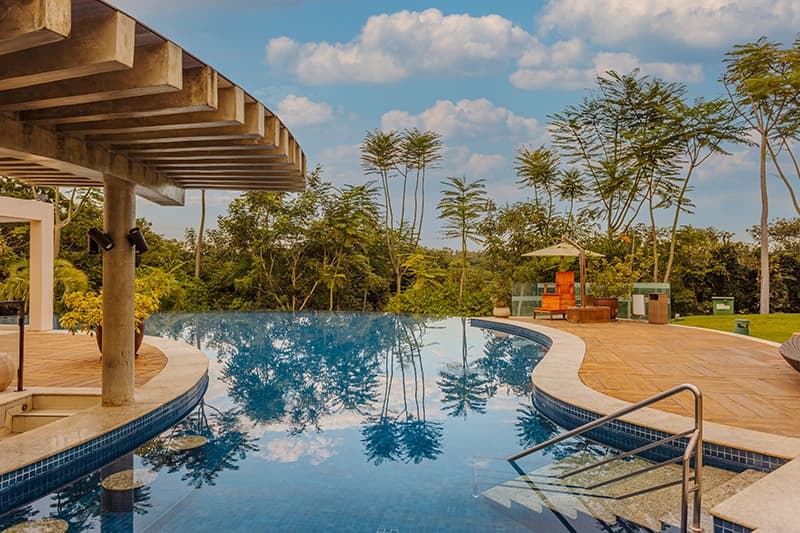 Vista superior da piscina com pergolado, deck e coqueiros.