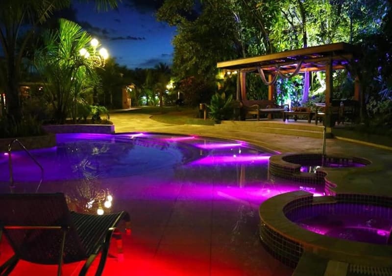 Piscina do resort com iluminação noturna colorida em tons de roxo e rosa.