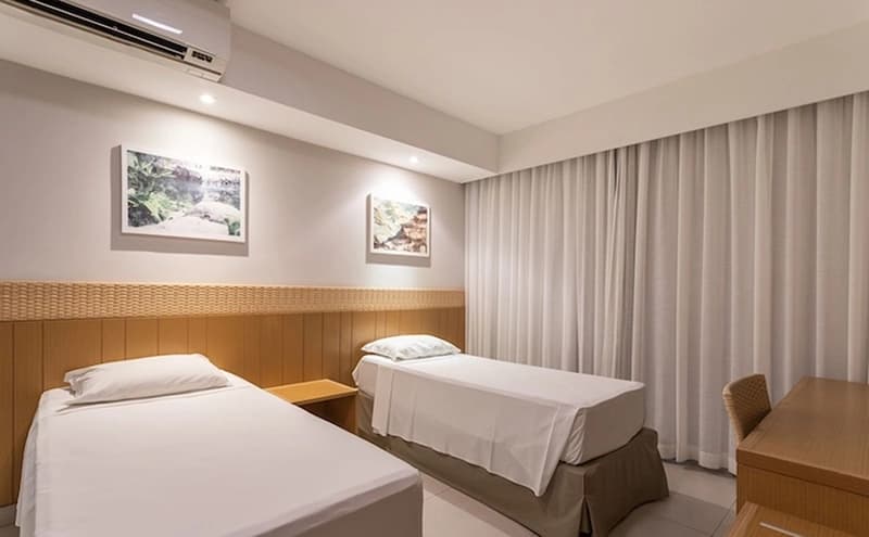 Quarto com duas camas de solteiro, cabeceiras de madeira e iluminação moderna.
