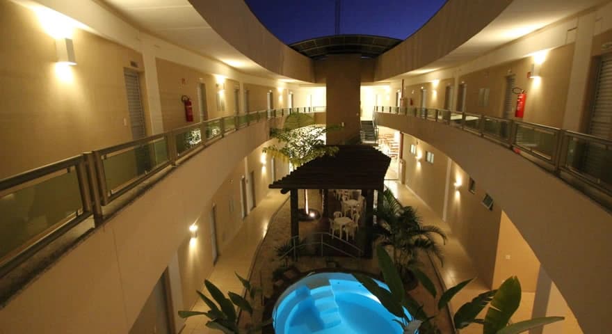 Piscina iluminada à noite com espreguiçadeiras.