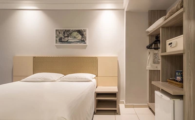 Acomodação com cama de casal e uma cabeceira branca embutida.