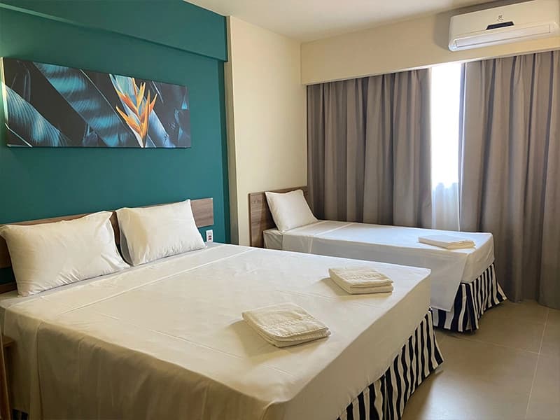 Quarto com cama de casal, lençóis brancos e parede verde.