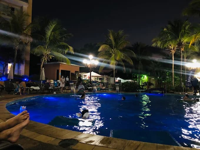 Hóspedes sentados em mesas na área da piscina durante a noite.