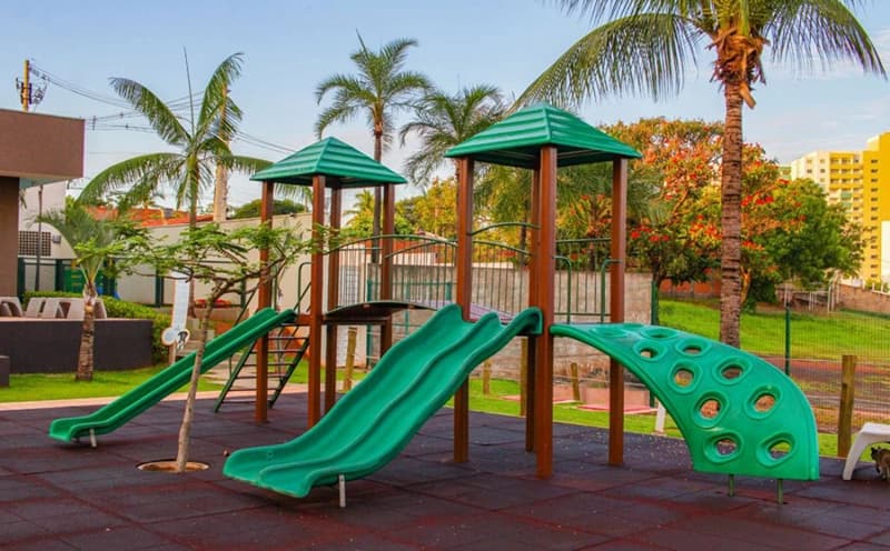 Playground externo com escorregadores verdes e estrutura de madeira.