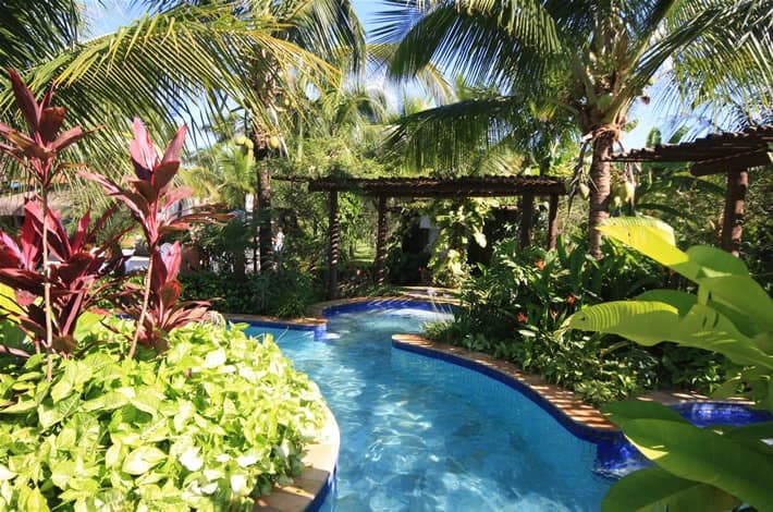 Piscina do resort com um pequeno toboágua e paisagismo exuberante.