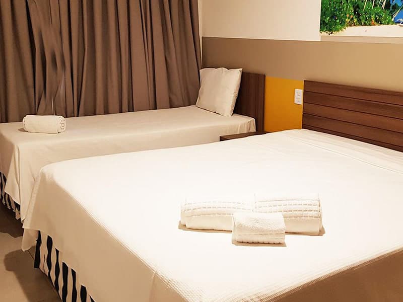 Quarto de casal com cama arrumada e cabeceira estofada.