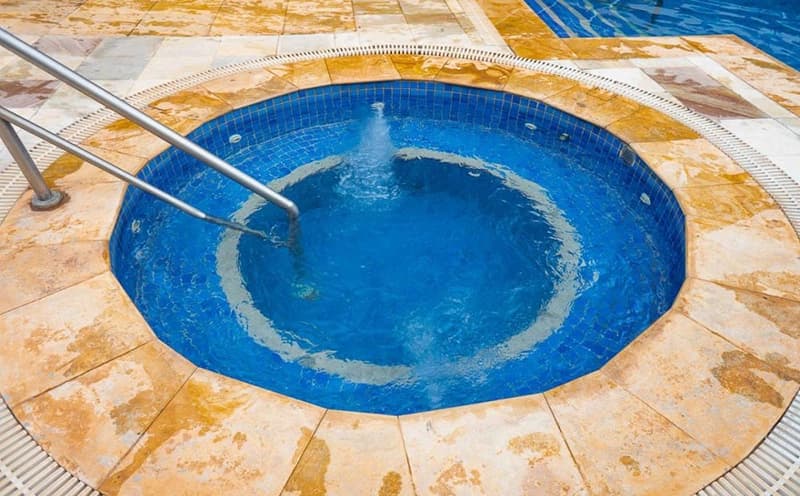 Ofurô redondo com pastilhas azuis e borda de pedra.