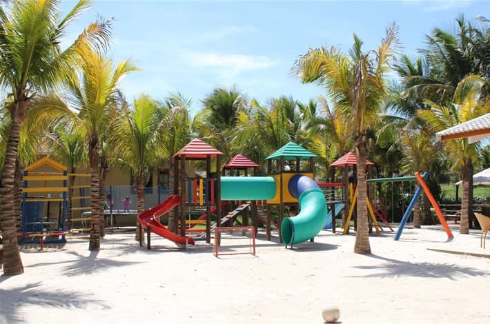 Playground infantil externo com escorregadores e brinquedos coloridos.
