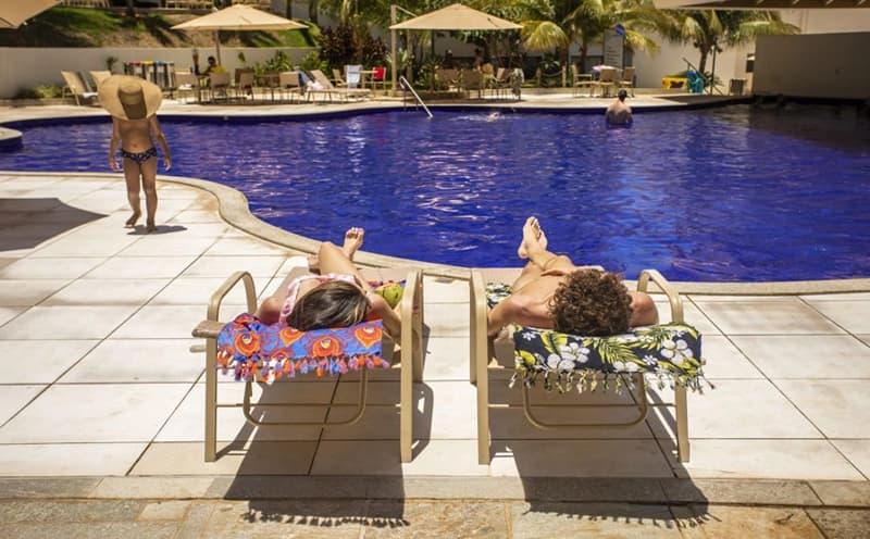 Hóspedes relaxando em espreguiçadeiras na beira da piscina.