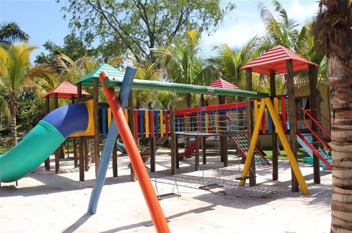 Parquinho infantil (playground) com vários brinquedos e piso de grama.