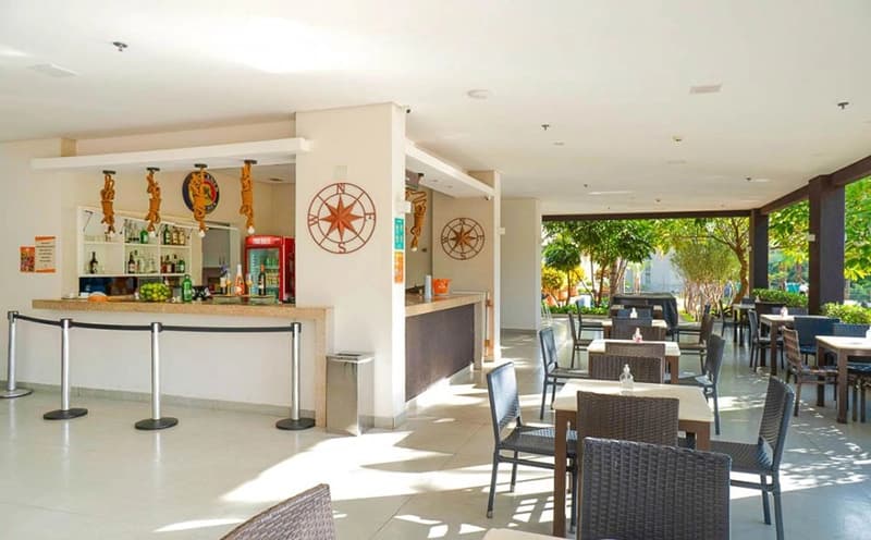 Balcão do bar do resort com cadeiras e prateleiras de bebidas.