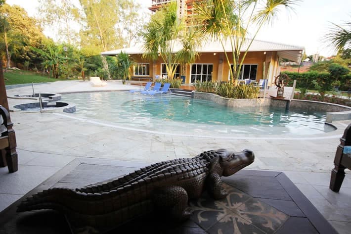 Piscina com uma grande estátua de jacaré e área verde ao redor.