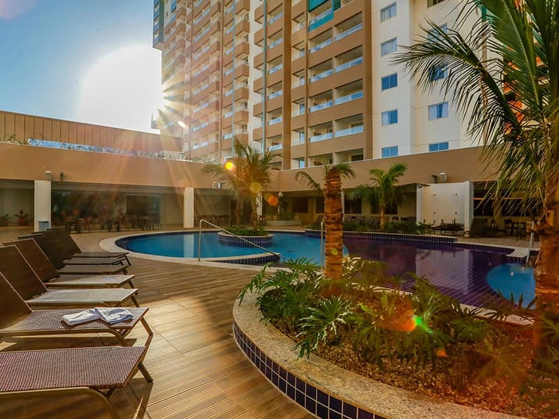 Vista da área da piscina com espreguiçadeiras e o prédio ao fundo.