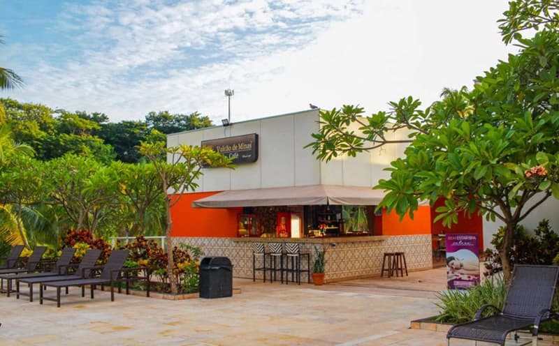 Área de restaurante externa com mesas, cadeiras e ombrelones.