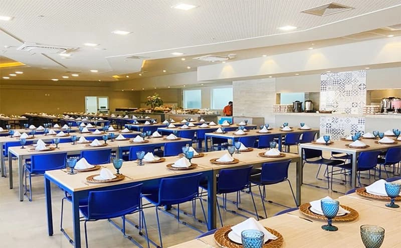 Amplo salão do restaurante com mesas postas e cadeiras azuis.