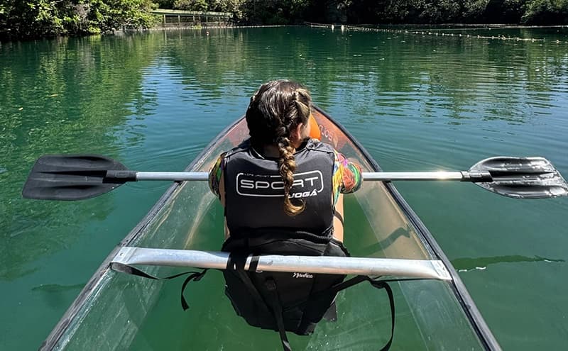 Turista em um caiaque transparente explorando o rio cercado por vegetação.