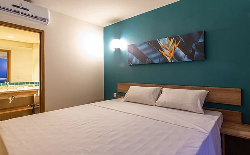 Quarto de casal com cabeceira estofada e iluminação ambiente.
