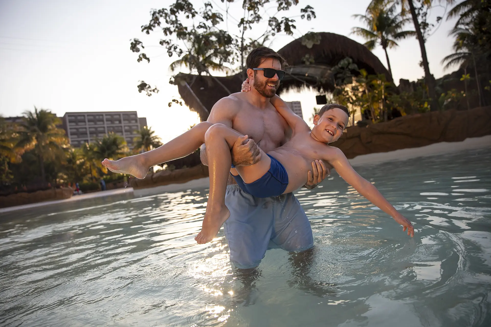 Pessoas se refrescando em uma piscina com um bar molhado ao fundo.
