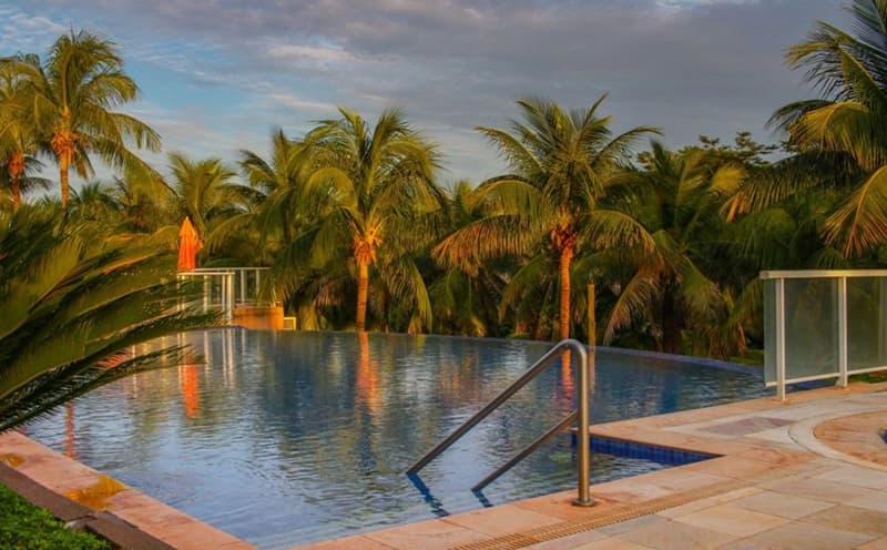 Piscina do resort cercada por coqueiros ao entardecer.