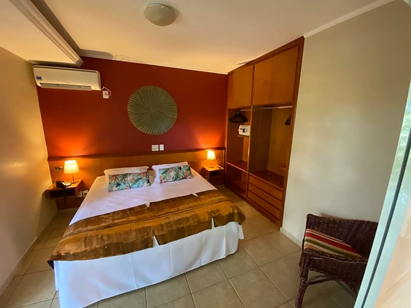 Quarto de hotel com cama arrumada e iluminação na cabeceira.