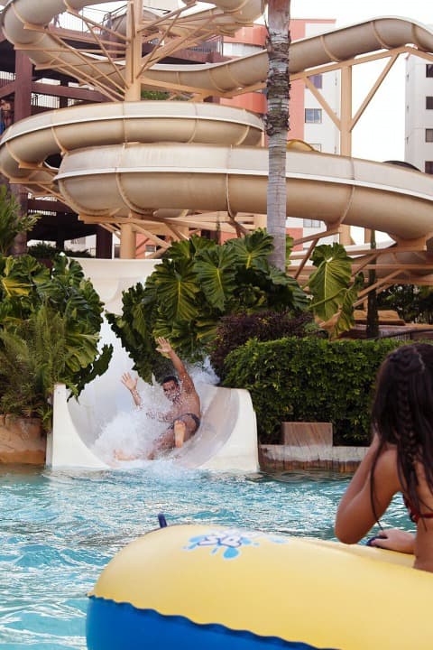 Criança sorrindo ao sair de um escorregador na piscina infantil.