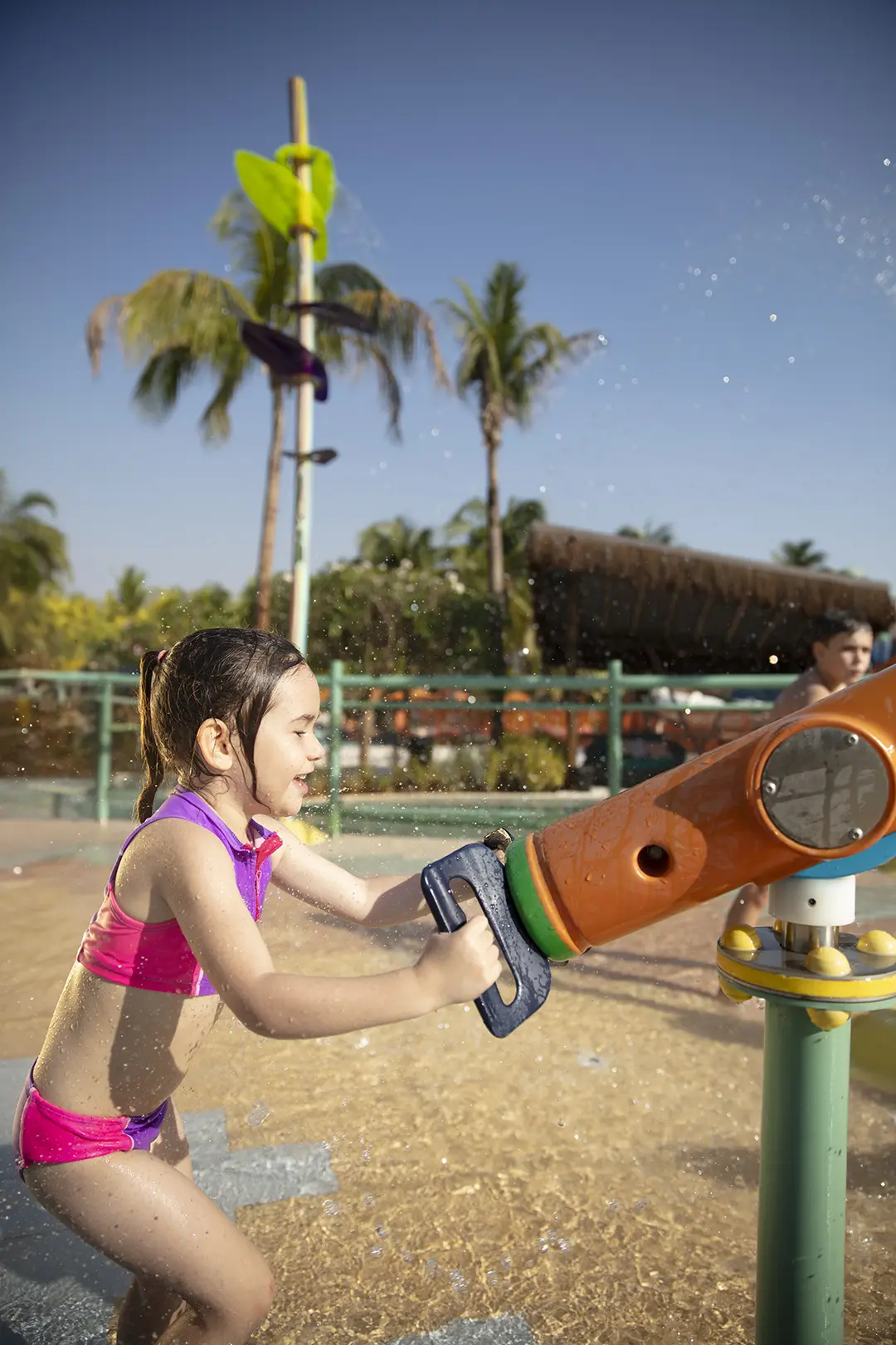 Pessoas em boias se divertindo em piscina com toboágua ao fundo.