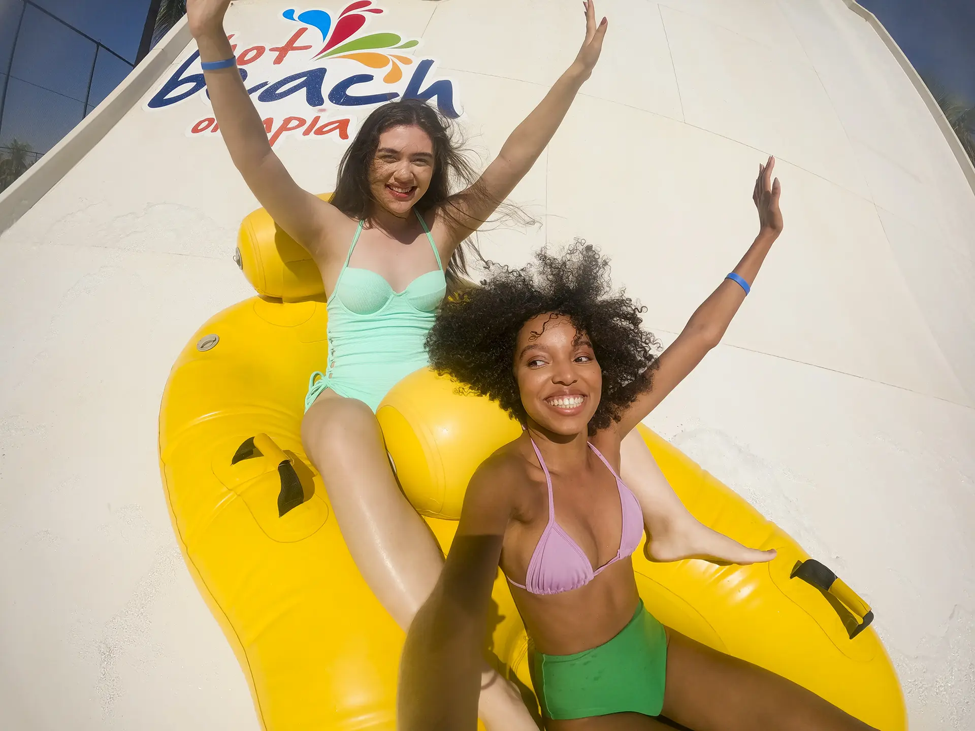 Dois amigos em boias amarelas, rindo enquanto descem o rio lento.