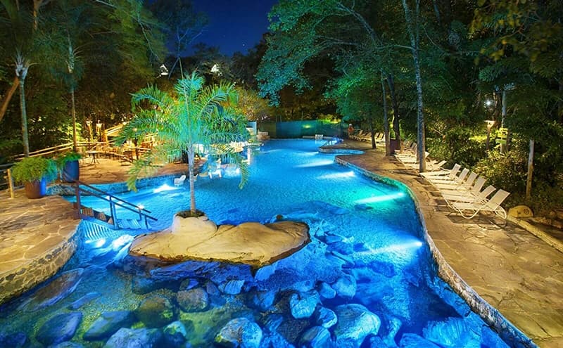 Pessoas relaxando no Parque das Fontes à noite, com iluminação especial