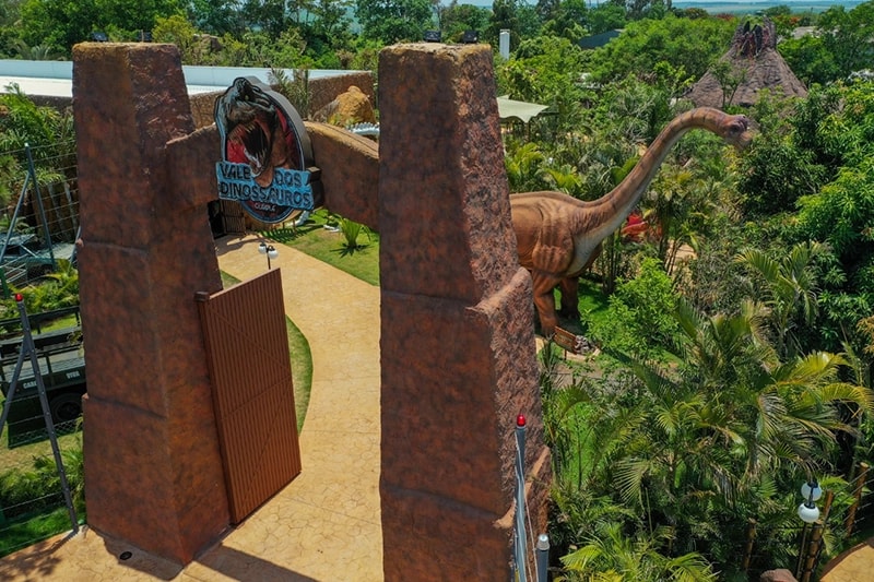 Banner principal do Vale dos Dinossauros mostrando diversas réplicas em cenário de floresta