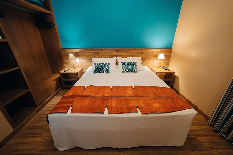 Quarto de hotel com duas camas, cabeceiras laranjas e iluminação azul.