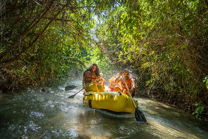 Pessoas relaxando em boias no rio lento, cercado pela mata nativa.
