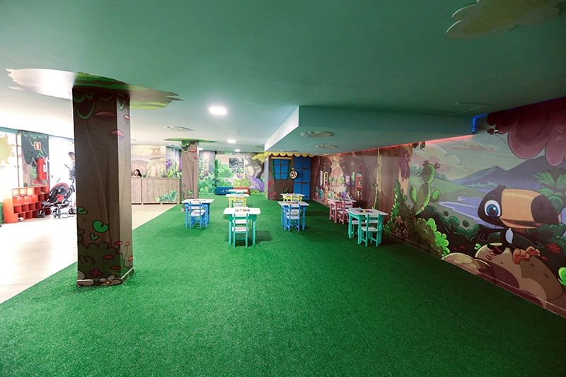 Área de recreação infantil interna, com piso verde e brinquedos.