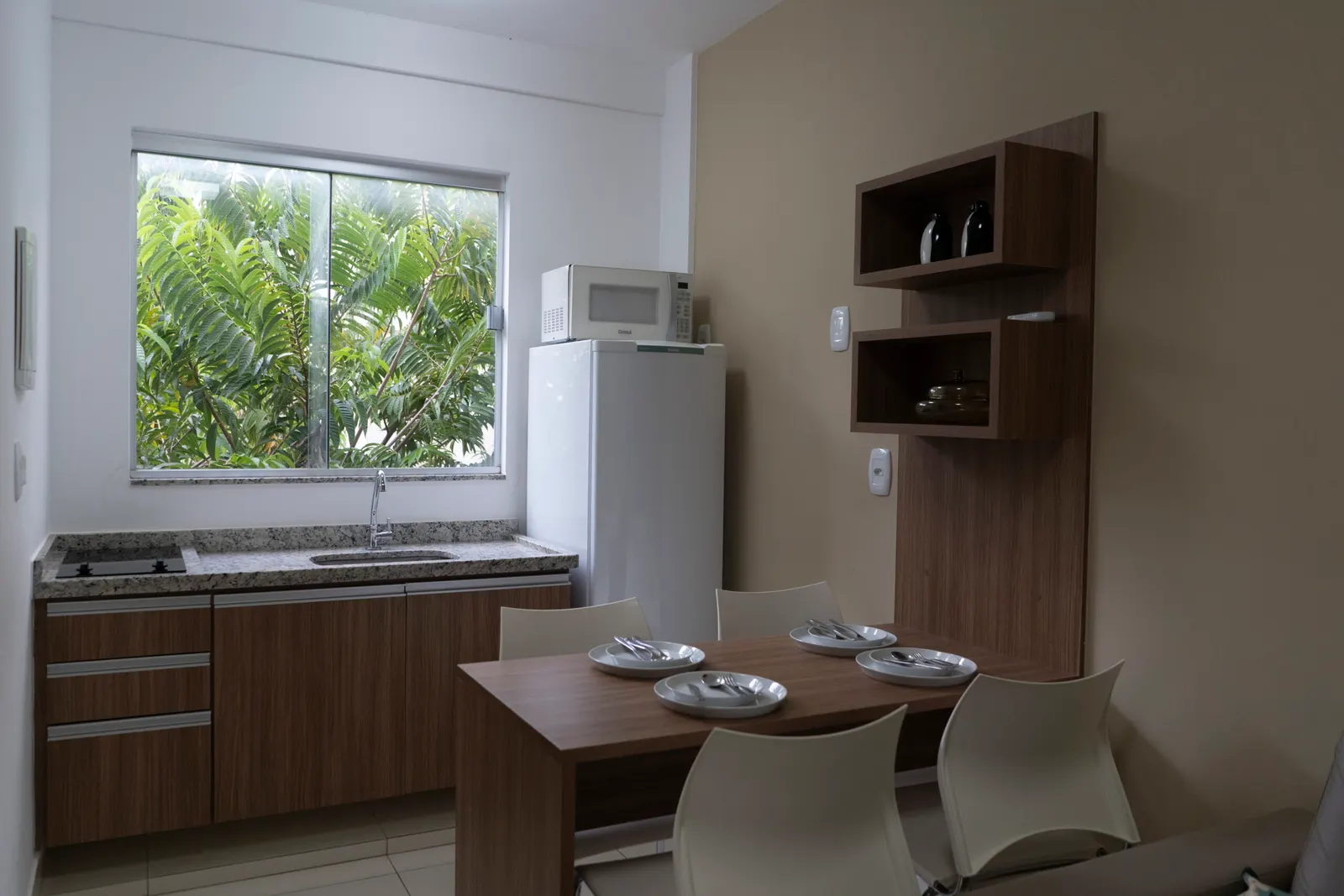 Cozinha compacta com geladeira, micro-ondas e mesa de refeições.