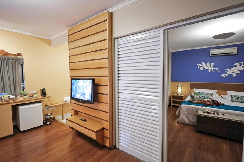 Quarto de hotel moderno com TV, frigobar e porta para o banheiro.