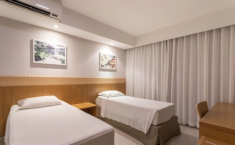 Quarto com duas camas de solteiro, cabeceiras de madeira e iluminação moderna.