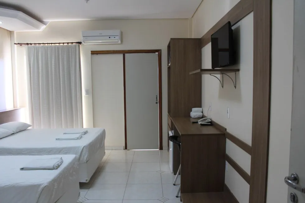 Quarto com TV de tela plana, frigobar e escrivaninha.