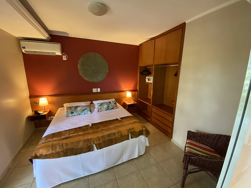 Quarto de hotel com cama arrumada e iluminação na cabeceira.