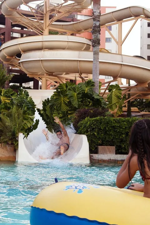 Criança sorrindo ao sair de um escorregador na piscina infantil.