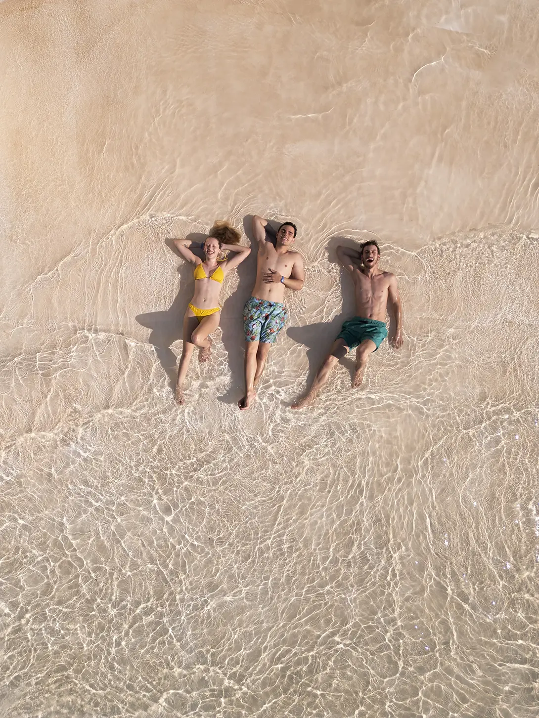 Grupo de amigos deitados na areia, sorrindo para uma foto tirada de cima.